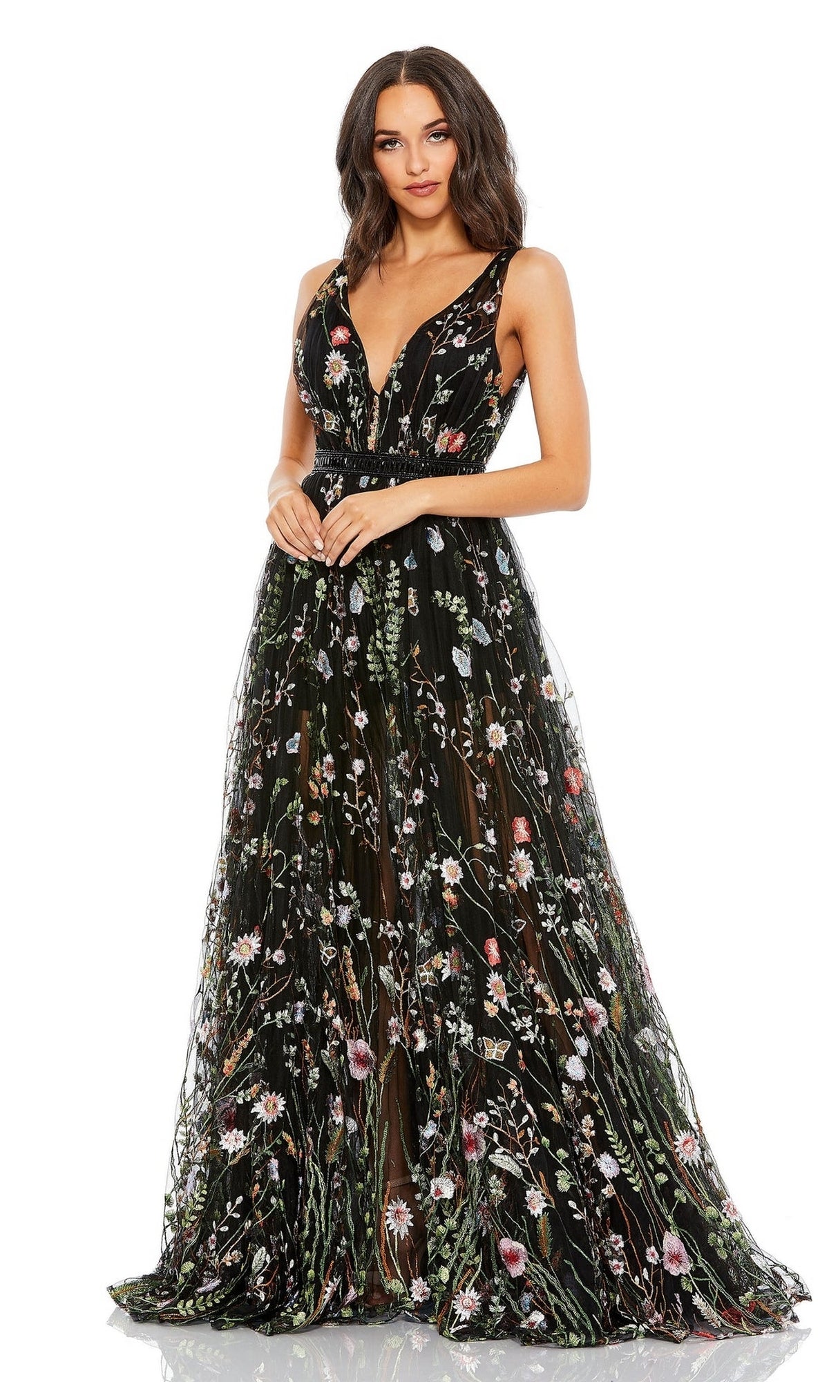 A woman stands facing forward in the Long Formal Dress 70132 by Mac Duggal—a sleeveless, floor-length black dress featuring a deep V-neck and colorful floral embroidery.
